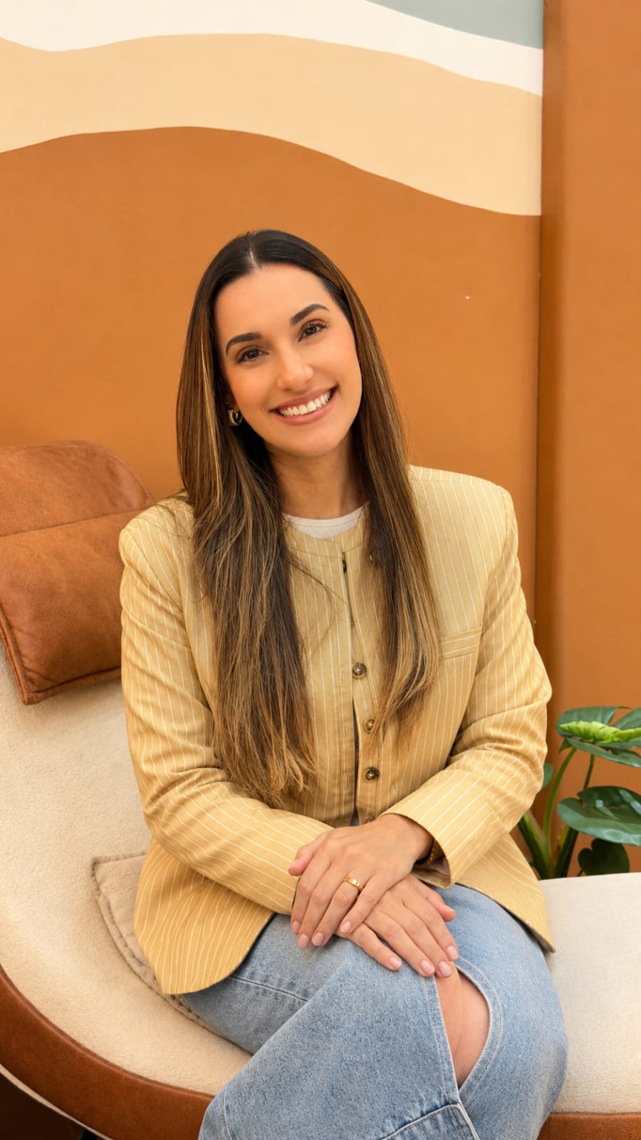 Caroline Viturino sentada em uma poltrona, com blazer amarelo