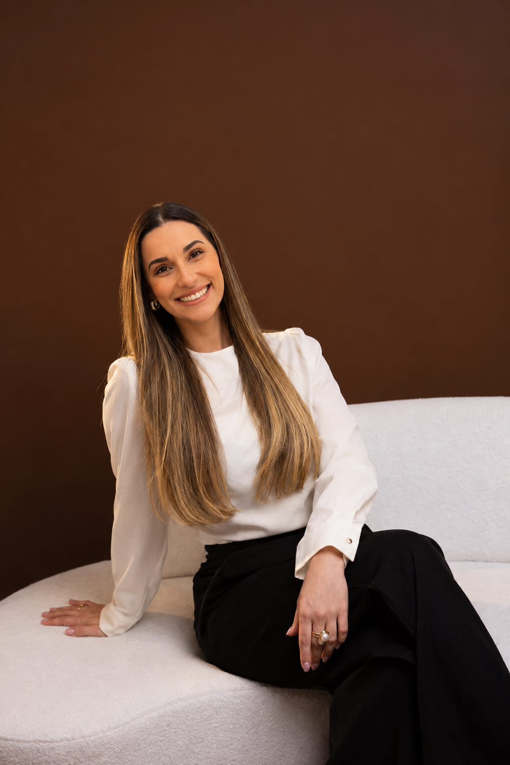 Caroline Viturino sorrindo, sentada em um sofá claro